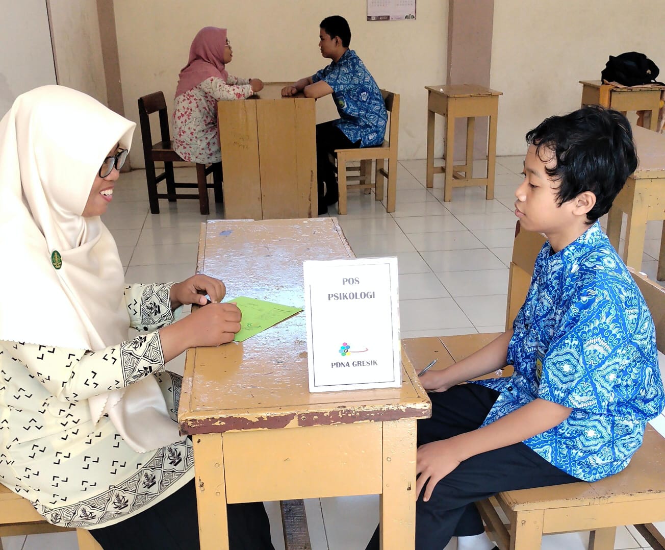 Tagar.co – Pada pos edukasi Pashmina Goes to School, Wakil Ketua PDNA Gresik yang membidangi Departemen Dakwah dan Pusintek Nurul Azizah, S.Psi. awalnya bertanya, "Siapa yang bawa botol berisi air?"

Beberapa siswa mengacungkan tangan. Perempuan yang akrab disapa Yunda Azizah itu memilih berjalan mendekati peserta perempuan yang duduk di tengah. Ia lalu meminjam botol tersebut dan membawanya ke depan, Kamis (18/7/2024) pagi.

Di hadapan 103 siswa kelas VII-IX SMP Muhammadiyah 4 Kebomas (Spemupat), Azizah kemudian menanyakan, "Siapa yang bisa menghancurkan air di depan ini tanpa menyentuhnya?" Botol itu ia angkat sejajar dengan matanya.

Para siswa saling menoleh. Mereka jadi bertanya-tanya. Sebagian tertawa penasaran. Seketika aula lantai 2 Spemupat riuh. Siswa diskusi antuasias.

Berselang semenit, Azizah memutuskan mengungkap dengan contoh langsung. "Hei air, kamu bodoh. Kamu itu tidak berguna!" Azizah memaki sambil menunjuk air dalam tumbler itu. Istighfar lantas terdengar dari para siswa.

Azizah melanjutkan merendahkan air tersebut. "Lihat temanmu bisa jalan-jalan. Bisa beli iPhone. Kamu miskin!"

Saat ditanya apakah percaya airnya hancur, di antara mereka banyak yang mengatakan tidak. Azizah membuktikan dengan hasil temuan lmuwan Jepang Dr. Masaru Emoto. Air yang mendapat afirmasi positif maka molekulnya tampak mengkristal. Sebaliknya, molekul air tampak rusak saat diebri ucapan negatif.

Begitu pula dengan manusia, katanya. Pada pos edukasi itu, Azizah mengajak mereka semua menyadari pentingnya menjaga lisan. Sebab, ucapan buruk bisa mudah menyakiti perasaan seseorang. Inilah salah satu pesan penting yang ia sampaikan saat berbagi tips menjaga kesehatan mental di era digital.

Baca Juga: Nasyiah Besuk Pantai Gresik, Temukan Sampah dari Rusia dan Ukraina 

Para kader Nasyiah dari PCNA Kebomas membantu pemberian real food berupa pisang, singkong dan telur rebus di Pos Gizi. (Tagar.co/Sayyidah Nuriyah)

Sehat Mental

Sebelumnya, para siswa juga antusias ketika Azizah mengajak mereka senam otak. Diiringi musik instrumental bertempo cepat, Azizah memeragakan beberapa gerakan kombinasi tangan dan mata. Guru maupun siswa semangat mengikuti gerakan Azizah.

Pasalnya, para siswa kompak mengangkat tangan saat Azizah menanyakan siapa yang sudah punya ponsel. Karena itulah, Azizah menekankan, "Mau tidak mau kita berdampingan dengan teknologi!"

Usai mengajak siswa Spemupat senam otak spesial Pashmina Goes to School, ia mulai mengenalkan kesehatan mental. "Sehat mental itu kondisi di mana kita bisa menghadapi stres. Bukan berarti orang sehat gak punya masalah. Yang sehat itu juga punya masalah tapi mampu menyelesaikan," ujarnya Azizah.

"Allah menciptakan manusia untuk diuji. Yang sehat mental bisa melewati ujian dengan baik. Bisa melakukan aktivitas sehari-hari secara produktif. Tidak hanya tidur saja. Ya mandi, belajar, makan, bersosialisasi, aktif memberi tanggapan dalam kelompok," imbuh Azizah.

Ia juga menegaskan, wajar jika mereka merasakan berbagai emosi. Setiap emosi punya manfaat. "Kadang sedih, bahagia, kecewa. Kalau cemas, gangguan nggak ya? Itu hal yang wajar! Jangan langsung, 'Kok aku cemas, kayaknya aku gangguan mental.' Cemas itu tanda. Perlu melakukan sesuatu agar tidak cemas," terangnya.

Karena para siswa sudah punya media sosial, Azizah mengungkap, "Yang bikin kita malas mandi ya HP." Gerr terdengar di antara siswa. Mereka menyetujuinya.

Di era digital ini, ia menyarankan agar mereka aktif bergerak. Selain itu, kalau ada masalah yang belum terselesaikan bisa konsultasi ke guru BK.

Baca Juga: Hafalan Haidar, Kolaborasi Indah Mugeb School dan Orang Tua

Salah satu siswi Spemupat sedang konsultasi ke dr Felisa Nur Khayana tentang IMT maupun kecenderungan anemia di Pos Kesehatan Pashmina PDNA Gresik. (Tagar.co/Sayyidah Nuriyah)

Kenalkan Nasyiah

Pos edukasi ini juga menjadi wadah untuk mengenalkan Nasyiatul Aisyiyah. Ketua Pimpinan Cabang Nasyiatul Aisyiyah (PCNA) Kebomas Nur Furrotul Muarrof, S.Pd.I. memimpin sesi ini.

"NA adalah organisasi otonom putri Muhammadiyah. Kalau Muhammadiyah ayahnya, Aisyiyah ibunya, NA putrinya," terang tim Pashmina ini di hadapan para Ikatan Pelajar Muhammadiyah Spemupat.

Di sisi lain, Wakil Ketua PDNA Gresik yang membidangi Departemen Kesehatan dan LHPB Maftuchatus Saidah, S.Pd menyampaikan terima kasih kepada Spemupat yang memberi kesempatan untuk menyapa adik-adik Ikatan Pelajar Muhammadiyah (IPM).

"Saya senang adik-adik IPM semangat menyanyikan mars NA. Adik-adik yang akan menjadi penerus Yunda-Yunda di Nasyiatul Aisyiyah ini," ujar Yunda Iid, sapaannya.

Kesempatan Pashmina Goes to School ini juga ia manfaatkan untuk mengajak remaja hidup sehat untuk mencegah stunting. Karena kesehatan tidak hanya mencakup psikologis tapi juga fisik.

"Sejak remaja boleh mengonsumsi tablet zat besi. Harus diimbangi makanan. Misal sayuran, buah, ikan, dan daging. Masakan di rumah insyaallah lebih sehat. Makan seblak dan cilok boleh tapi porsinya dikurangi," tuturnya.

Baca Juga: Masa Depan Bumi tanpa Kantong Plastik, Inovasi dan Solusi

Lima Pos

Tak hanya pos edukasi. PDNA Gresik juga menggelar lima pos Pashmina Goes to School. Ada pos registrasi di mana setiap siswa mendapat Kartu Pashmina. Pos ini terletak di sisi tangga. Jadi peserta wajib mampir ke pos ini sebelum menuju pos edukasi di lantai 2.

Kartu Pashmina wajib siswa bawa ketika memasuki setiap pos. Di sana terdapat kolom untuk mencatat identitas diri maupun informasi yang mereka peroleh selama mengikuti masing-masing pos.

Ada pula pos kesehatan. Lokasinya di ruang kelas VIII. Di sini PDNA Gresik menggandeng 1 dokter dan 2 perawat dari Rumah Sakit Muhammadiyah Gresik (RSMG). Tim Pashmina PDNA Gresik Mawaddatin, S.Kep.Ners. dan dua guru juga turut membantu.

Di sini siswa bisa mengecek tekanan darah juga berat dan tinggi badannya untuk mengetahui Indeks Massa Tubuh (IMT). Fasilitas lainnya adalah konsultasi kesehatan dengan dokter.

Usai melayani siswa, dr Felisa Nur Khayana mengungkap, hanya beberapa siswa yang Anemia. "Bisa konsumsi tablet tambah darah dan perbanyak makan buah sayur," sarannya. 

Dari penghitungan IMT, lanjutnya, para siswa rata-rata memiliki berat badan ideal. "Ada obesitas beberapa. Yang kekurangan berat badan cuma sedikit," ungkapnya.

Beberapa siswa sedang konseling bersama Yunda-Yunda PDNA Gresik di Pos Psikologi. (Tagar.co/Sayyidah Nuriyah)

Respon Positif

Di sampingnya, ruang kelas IX, ada pos konseling. Di sini ada dua anggota Pashmina berlatar psikologi yang siap menyimak curhatan para siswa. Ada Sayyidah Nuriyah, S.Psi dan Lu'luatul Usroh, S.Psi. Meski awalnya banyak siswa yang malu dan ragu, pada akhirnya belasan siswa mau konseling.

Wakil Kepala Kurikulum Spemupat Lendra Aditya Wardhana, S.Pd menyambut baik pos-pos Pashmina Goes to School ini. Ia mengajak siswa berani mencurahkan isi hatinya (curhat).

"Bisa cerita ya. Mungkin selama ini dipendam, tidak bisa diungkap secara langsung sampai mengganggu aktivitas sehari-hari," ujarnya.

"Teman yang suka tertawa belum tentu di hatinya ikut tertawa. Bisa jadi ada masalah yang ingin dia sampaikan tapi dia tutupi dengan keceriaan. Manfaatkan kesempatan hari ini," imbuhnya.

Terakhir, pos gizi. Di sinilah para kader Nasyiah PCNA Kebomas, sebagai panitia lokal, sigap membagikan makanan kepada para siswa. Seperti sebutir telur, sepotong singkong, dan sebuah pisang hijau. Siswa membawa kotak makan sendiri untuk mengurangi sampah plastik sekali pakai.

Agenda ini juga berkolaborasi dengan kader IPM Spemupat. Ada Nikita Alfina Syahriani kelas IX sebagai pembawa acara, Naila Anisa Latifah kelas VIII pembaca tilawah, dan Almira Shafa Desyanti kelas IX sebagai dirigen. (#)

Jurnalis Sayyidah Nuriyah Penyunting Mohammad Nurfatoni