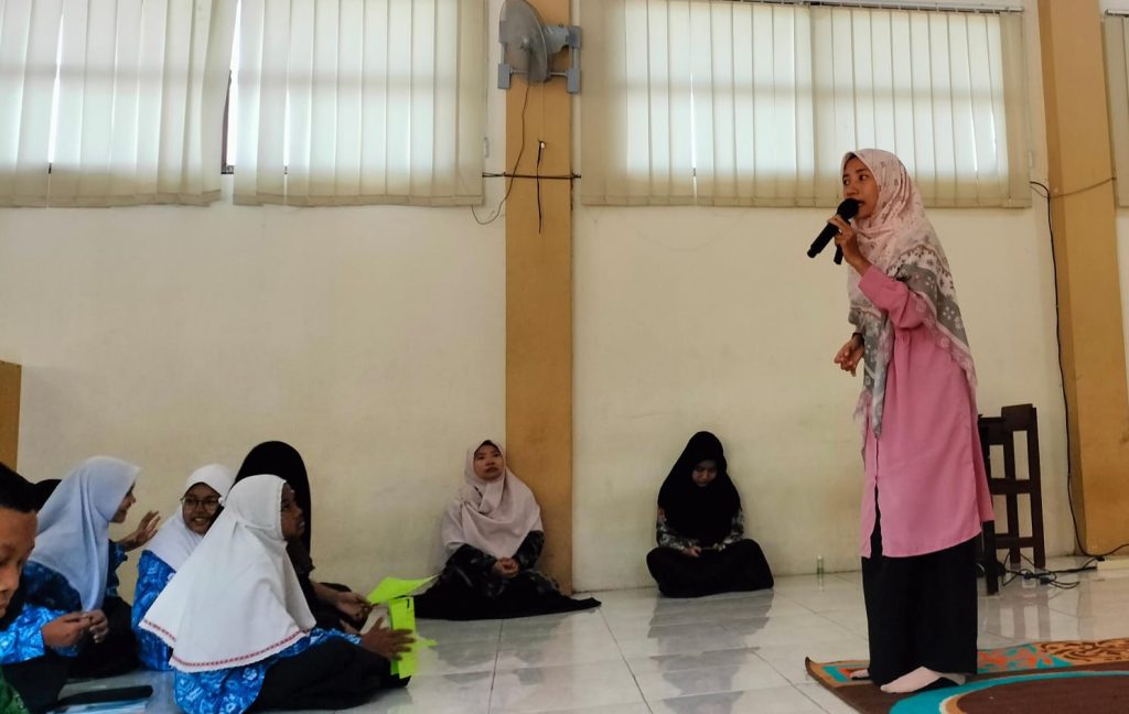 Tagar.co – Pada pos edukasi Pashmina Goes to School, Wakil Ketua PDNA Gresik yang membidangi Departemen Dakwah dan Pusintek Nurul Azizah, S.Psi. awalnya bertanya, "Siapa yang bawa botol berisi air?"

Beberapa siswa mengacungkan tangan. Perempuan yang akrab disapa Yunda Azizah itu memilih berjalan mendekati peserta perempuan yang duduk di tengah. Ia lalu meminjam botol tersebut dan membawanya ke depan, Kamis (18/7/2024) pagi.

Di hadapan 103 siswa kelas VII-IX SMP Muhammadiyah 4 Kebomas (Spemupat), Azizah kemudian menanyakan, "Siapa yang bisa menghancurkan air di depan ini tanpa menyentuhnya?" Botol itu ia angkat sejajar dengan matanya.

Para siswa saling menoleh. Mereka jadi bertanya-tanya. Sebagian tertawa penasaran. Seketika aula lantai 2 Spemupat riuh. Siswa diskusi antuasias.

Berselang semenit, Azizah memutuskan mengungkap dengan contoh langsung. "Hei air, kamu bodoh. Kamu itu tidak berguna!" Azizah memaki sambil menunjuk air dalam tumbler itu. Istighfar lantas terdengar dari para siswa.

Azizah melanjutkan merendahkan air tersebut. "Lihat temanmu bisa jalan-jalan. Bisa beli iPhone. Kamu miskin!"

Saat ditanya apakah percaya airnya hancur, di antara mereka banyak yang mengatakan tidak. Azizah membuktikan dengan hasil temuan lmuwan Jepang Dr. Masaru Emoto. Air yang mendapat afirmasi positif maka molekulnya tampak mengkristal. Sebaliknya, molekul air tampak rusak saat diebri ucapan negatif.

Begitu pula dengan manusia, katanya. Pada pos edukasi itu, Azizah mengajak mereka semua menyadari pentingnya menjaga lisan. Sebab, ucapan buruk bisa mudah menyakiti perasaan seseorang. Inilah salah satu pesan penting yang ia sampaikan saat berbagi tips menjaga kesehatan mental di era digital.

Baca Juga: Nasyiah Besuk Pantai Gresik, Temukan Sampah dari Rusia dan Ukraina 

Para kader Nasyiah dari PCNA Kebomas membantu pemberian real food berupa pisang, singkong dan telur rebus di Pos Gizi. (Tagar.co/Sayyidah Nuriyah)

Sehat Mental

Sebelumnya, para siswa juga antusias ketika Azizah mengajak mereka senam otak. Diiringi musik instrumental bertempo cepat, Azizah memeragakan beberapa gerakan kombinasi tangan dan mata. Guru maupun siswa semangat mengikuti gerakan Azizah.

Pasalnya, para siswa kompak mengangkat tangan saat Azizah menanyakan siapa yang sudah punya ponsel. Karena itulah, Azizah menekankan, "Mau tidak mau kita berdampingan dengan teknologi!"

Usai mengajak siswa Spemupat senam otak spesial Pashmina Goes to School, ia mulai mengenalkan kesehatan mental. "Sehat mental itu kondisi di mana kita bisa menghadapi stres. Bukan berarti orang sehat gak punya masalah. Yang sehat itu juga punya masalah tapi mampu menyelesaikan," ujarnya Azizah.

"Allah menciptakan manusia untuk diuji. Yang sehat mental bisa melewati ujian dengan baik. Bisa melakukan aktivitas sehari-hari secara produktif. Tidak hanya tidur saja. Ya mandi, belajar, makan, bersosialisasi, aktif memberi tanggapan dalam kelompok," imbuh Azizah.

Ia juga menegaskan, wajar jika mereka merasakan berbagai emosi. Setiap emosi punya manfaat. "Kadang sedih, bahagia, kecewa. Kalau cemas, gangguan nggak ya? Itu hal yang wajar! Jangan langsung, 'Kok aku cemas, kayaknya aku gangguan mental.' Cemas itu tanda. Perlu melakukan sesuatu agar tidak cemas," terangnya.

Karena para siswa sudah punya media sosial, Azizah mengungkap, "Yang bikin kita malas mandi ya HP." Gerr terdengar di antara siswa. Mereka menyetujuinya.

Di era digital ini, ia menyarankan agar mereka aktif bergerak. Selain itu, kalau ada masalah yang belum terselesaikan bisa konsultasi ke guru BK.

Baca Juga: Hafalan Haidar, Kolaborasi Indah Mugeb School dan Orang Tua

Salah satu siswi Spemupat sedang konsultasi ke dr Felisa Nur Khayana tentang IMT maupun kecenderungan anemia di Pos Kesehatan Pashmina PDNA Gresik. (Tagar.co/Sayyidah Nuriyah)

Kenalkan Nasyiah

Pos edukasi ini juga menjadi wadah untuk mengenalkan Nasyiatul Aisyiyah. Ketua Pimpinan Cabang Nasyiatul Aisyiyah (PCNA) Kebomas Nur Furrotul Muarrof, S.Pd.I. memimpin sesi ini.

"NA adalah organisasi otonom putri Muhammadiyah. Kalau Muhammadiyah ayahnya, Aisyiyah ibunya, NA putrinya," terang tim Pashmina ini di hadapan para Ikatan Pelajar Muhammadiyah Spemupat.

Di sisi lain, Wakil Ketua PDNA Gresik yang membidangi Departemen Kesehatan dan LHPB Maftuchatus Saidah, S.Pd menyampaikan terima kasih kepada Spemupat yang memberi kesempatan untuk menyapa adik-adik Ikatan Pelajar Muhammadiyah (IPM).

"Saya senang adik-adik IPM semangat menyanyikan mars NA. Adik-adik yang akan menjadi penerus Yunda-Yunda di Nasyiatul Aisyiyah ini," ujar Yunda Iid, sapaannya.

Kesempatan Pashmina Goes to School ini juga ia manfaatkan untuk mengajak remaja hidup sehat untuk mencegah stunting. Karena kesehatan tidak hanya mencakup psikologis tapi juga fisik.

"Sejak remaja boleh mengonsumsi tablet zat besi. Harus diimbangi makanan. Misal sayuran, buah, ikan, dan daging. Masakan di rumah insyaallah lebih sehat. Makan seblak dan cilok boleh tapi porsinya dikurangi," tuturnya.

Baca Juga: Masa Depan Bumi tanpa Kantong Plastik, Inovasi dan Solusi

Lima Pos

Tak hanya pos edukasi. PDNA Gresik juga menggelar lima pos Pashmina Goes to School. Ada pos registrasi di mana setiap siswa mendapat Kartu Pashmina. Pos ini terletak di sisi tangga. Jadi peserta wajib mampir ke pos ini sebelum menuju pos edukasi di lantai 2.

Kartu Pashmina wajib siswa bawa ketika memasuki setiap pos. Di sana terdapat kolom untuk mencatat identitas diri maupun informasi yang mereka peroleh selama mengikuti masing-masing pos.

Ada pula pos kesehatan. Lokasinya di ruang kelas VIII. Di sini PDNA Gresik menggandeng 1 dokter dan 2 perawat dari Rumah Sakit Muhammadiyah Gresik (RSMG). Tim Pashmina PDNA Gresik Mawaddatin, S.Kep.Ners. dan dua guru juga turut membantu.

Di sini siswa bisa mengecek tekanan darah juga berat dan tinggi badannya untuk mengetahui Indeks Massa Tubuh (IMT). Fasilitas lainnya adalah konsultasi kesehatan dengan dokter.

Usai melayani siswa, dr Felisa Nur Khayana mengungkap, hanya beberapa siswa yang Anemia. "Bisa konsumsi tablet tambah darah dan perbanyak makan buah sayur," sarannya. 

Dari penghitungan IMT, lanjutnya, para siswa rata-rata memiliki berat badan ideal. "Ada obesitas beberapa. Yang kekurangan berat badan cuma sedikit," ungkapnya.

Beberapa siswa sedang konseling bersama Yunda-Yunda PDNA Gresik di Pos Psikologi. (Tagar.co/Sayyidah Nuriyah)

Respon Positif

Di sampingnya, ruang kelas IX, ada pos konseling. Di sini ada dua anggota Pashmina berlatar psikologi yang siap menyimak curhatan para siswa. Ada Sayyidah Nuriyah, S.Psi dan Lu'luatul Usroh, S.Psi. Meski awalnya banyak siswa yang malu dan ragu, pada akhirnya belasan siswa mau konseling.

Wakil Kepala Kurikulum Spemupat Lendra Aditya Wardhana, S.Pd menyambut baik pos-pos Pashmina Goes to School ini. Ia mengajak siswa berani mencurahkan isi hatinya (curhat).

"Bisa cerita ya. Mungkin selama ini dipendam, tidak bisa diungkap secara langsung sampai mengganggu aktivitas sehari-hari," ujarnya.

"Teman yang suka tertawa belum tentu di hatinya ikut tertawa. Bisa jadi ada masalah yang ingin dia sampaikan tapi dia tutupi dengan keceriaan. Manfaatkan kesempatan hari ini," imbuhnya.

Terakhir, pos gizi. Di sinilah para kader Nasyiah PCNA Kebomas, sebagai panitia lokal, sigap membagikan makanan kepada para siswa. Seperti sebutir telur, sepotong singkong, dan sebuah pisang hijau. Siswa membawa kotak makan sendiri untuk mengurangi sampah plastik sekali pakai.

Agenda ini juga berkolaborasi dengan kader IPM Spemupat. Ada Nikita Alfina Syahriani kelas IX sebagai pembawa acara, Naila Anisa Latifah kelas VIII pembaca tilawah, dan Almira Shafa Desyanti kelas IX sebagai dirigen. (#)

Jurnalis Sayyidah Nuriyah Penyunting Mohammad Nurfatoni