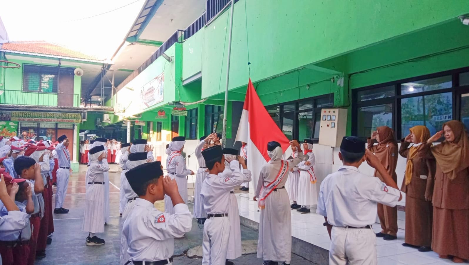 Tagar.co – Barisan siswa berseragam merah putih, bertopi warna senada dan berdasi merah terlihat rapi. Gerakan mereka selaras dengan panduan pembina upacara yang memimpin jalannya upacara di halaman SD Negeri Bulak Rukem 1 Surabaya, Senin (29/7/2024). Mereka sudah masuk di area lapangan sejak pukul 6.15 WIB. Upacara bendera tiap Senin itu dimulai tepat ketika jarum jam menunjukkan pukul 6.30 WIB. Tepat ketika hendak mulai, tiba-tiba dua anak laki-laki berlarian pontang panting menuju barisan. Sambil terengah-engah, mereka membetulkan letak dasi dan topinya. Ialah Azel Fedora Isatitaah (10) dan Barnes Fasle Maula (10). Tak mereka hiraukan peserta upacara yang memandang dengan penuh tanya. Begitupun dengan pandangan para guru yang turut berdiri di barisan depan siswa, berdampingan dengan para petugas upacara berseragam putih di barisan depan. Pemeriksaan kelengkapan atribut sekolah menjadi awal kesiapan barisan yang dipimpin oleh pemimpin barisan. Harapannya, anggota memeriksa kelengkapan seragam sekolahnya. Mulai dari topi, dasi, baju putih dengan badge kelas di lengan kanan, nama lengkap di dada kanan dan logo Tut Wuri Handayani di saku kiri. Selain itu, memakai ikat pinggang berlogo SD. Juga bawahan rok untuk siswa perempuan dan celana untuk siswa laki-laki. Berakhir pada kaos kaki putih dan sepatu hitam. Para siswa memeriksa semua itu sesuai instruksi Chairul Anwar, Wali Kelas VI E. Dia yang pagi itu mendapat amanah mengatur kesiapan peserta sebelum upacara resmi dimulai. "Hari ini yang atributnya belum lengkap masih kita beri waktu untuk dilengkapi hingga Senin depan. Bagi yang belum punya, bisa beli di koperasi sekolah agar seragam kalian rapi," pesannya di tengah depan lapangan. Sejenak suasana hening ketika Achmad Maulana Rahmatullah (11), bertugas sebagai pemimpin upacara, menyiapkan barisan. "Seluruhnya, siap grak!" tegasnya lantang. Satu per satu petugas upacara menjalankan tugasnya. Hingga tiba giliran Paskibraka mengibarkan sang Merah Putih dengan kompak. Mereka menjalankan tugasnya sampai bendera Indonesia berkibar di angkasa. Santri Surabaya Juara FASI XII Diterima Sekda Disiplin dari Rumah Upacara hari Senin yang sudah menjadi rutinitas sekolah itu punya peserta baru. Mereka yang sebelumnya kelas IV masuk siang, kini naik kelas V dan masuk pagi. Jadi ada perubahan pembiasaan yang membuat siswa perlu menyiapkan diri. Pagi itu, yang menjadi pembina upacara ialah Masbuchin, guru mata pelajaran Pendidikan Agama Islam dan Budi pekerti. Kesempatan menyampaikan amanat upacara ia manfaatkan untuk menekankan pesan moral terkait kedisiplinan. "Selamat untuk siswa kelas IV yang naik kelas V dan yang kelas V naik kelas VI. Khususnya kelas V yang semula di kelas IV masuk siang, sekarang di kelas V masuk pagi," sapanya di awal. Kepada siswa kelas V, Masbuchin mengharuskan mereka mulai menata pola tidur dan disiplin waktu. Harapannya, mereka bisa datang tepat waktu ke sekolah. Lebih lanjut, ia mengatakan, "Mulai hari ini, setiap Senin akan ada upacara. Maka sejak pukul 6.30 seluruh siswa sudah harus di lapangan berbaris rapi untuk melatih kedisiplinan dan kemandirian kalian." Latihan kedisiplinan ini menurutnya dimulai dari menyiapkan diri ketika di rumah. "Berawal dari istirahat yang cukup, menyiapkan jadwal pelajaran, dan seragam sekolah malam hari di rumah," urainya. Dengan disiplin sejak di rumah, ia meyakini, esok paginya anak-anak lebih siap ke sekolah. (#) Jurnalis Tri Eko Sulistiowati Penyunting Sayyidah Nuriyah