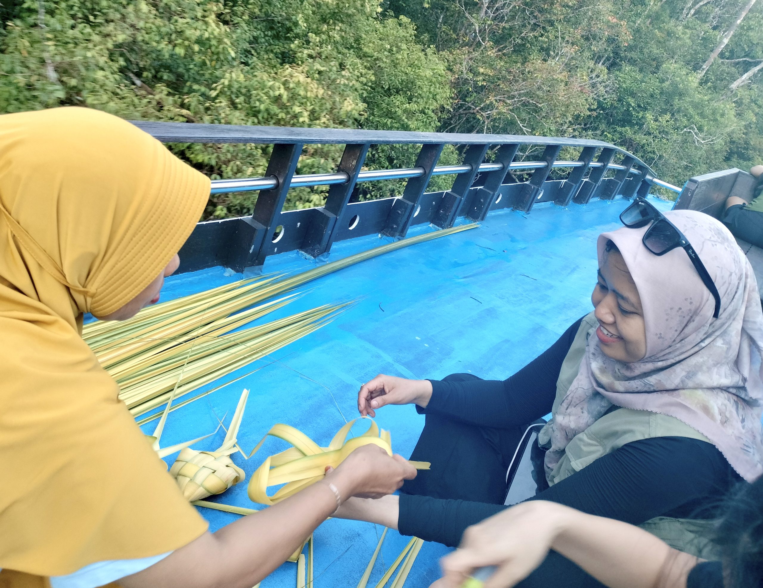 Menikmati senja di Sungai Sekonyer, wisatawan ikut belajar menganyam ketupat tulak bala dari Acil Masnih di rooftop kelotok. Akhirnya terpecahkan perbedaan cara menganyam ketupat laki-laki dan perempuan.