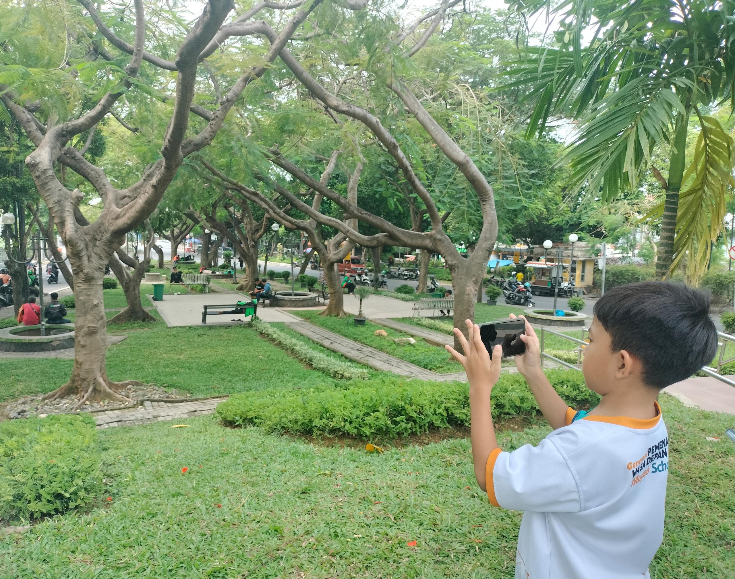Siswa SD Muhammadiyah 1 GKB Gresik perdana kelas luar ruang. Belajar fokus, komposisi, hingga teknik fotografi levitasi dan frog eyes di Taman Bundaran GKB.